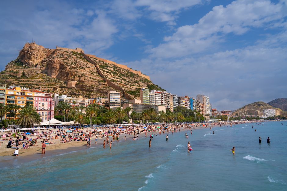 Crowded beach in Alicante with views of Santa Bárbara Castle. Ideal summer scene.